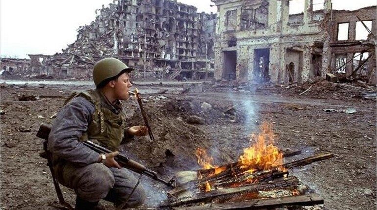 солдат прикуривает от костра, солдат на пожарище в разрушенном городе