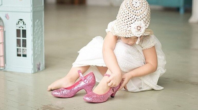 маленькая девочка одевает туфли взрослых, ребенок надевает мамины туфли