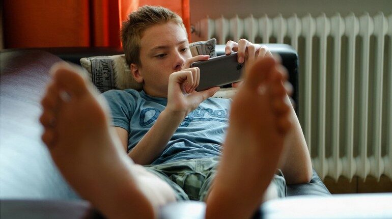 мальчик лежит и смотрит в телефон, подросток смотрит в смартфон