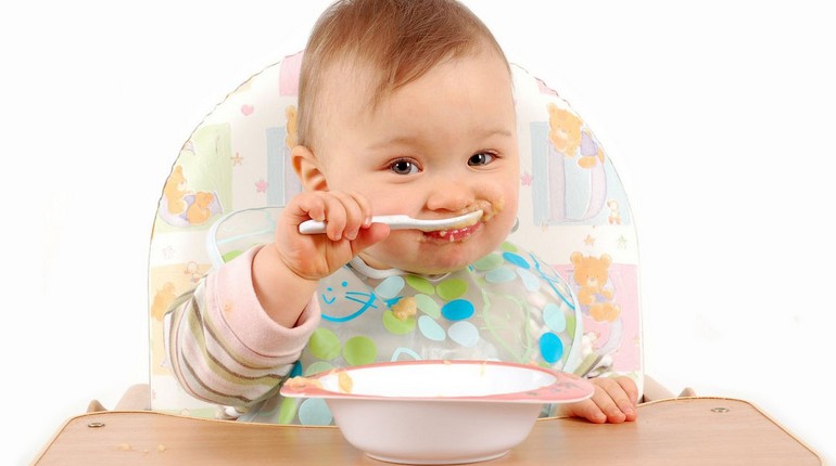 малыш сам кушает с ложечки, ребенок сидит в стульчике для кормления и кушает ложкой, младенец кушает 
