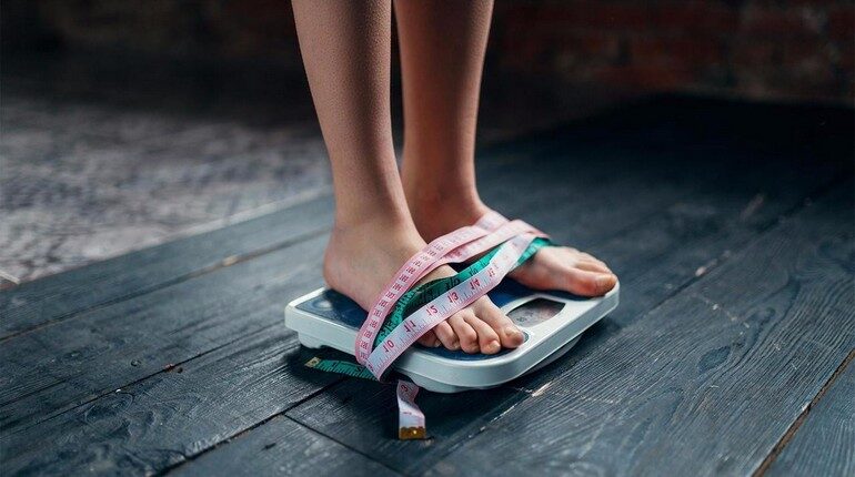 ноги девушки стоят на весах обмотаны сантиметровой лентой, мотивация к снижению веса